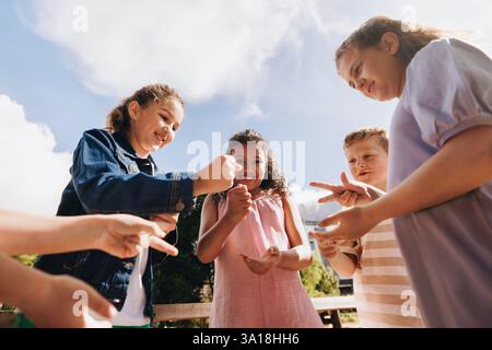 Un gruppo di bambini diversi impegnati in un divertente gioco di forbici da roccia all'aperto. Sembrano felici e animati, godendosi il loro tempo insieme sotto Foto Stock