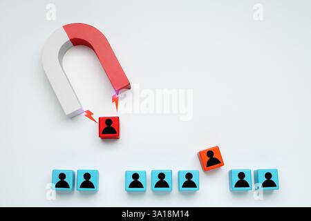 Magnete che attrae uno dei cubi di legno con figure umane su sfondo bianco, vista dall'alto. Reclutamento o acquisizione di clienti Foto Stock