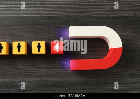 Magnete che attrae cubi con figure umane su sfondo in legno, vista dall'alto. Reclutamento o acquisizione di clienti Foto Stock