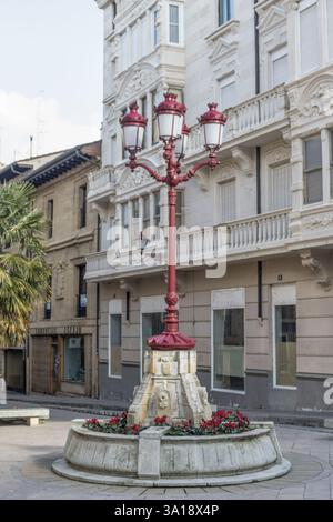 Lampione rosso decorativo con piedistallo in pietra e disposizione floreale in Plaza de la Paz, Haro, Spagna. Foto Stock