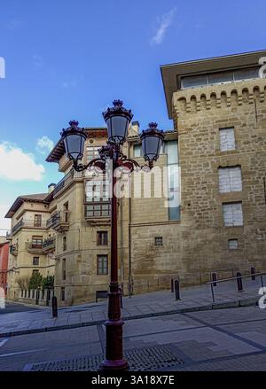 Lampada da strada decorativa in ferro battuto a Haro, Spagna, con una torre medievale in pietra e edifici storici sullo sfondo. Foto Stock