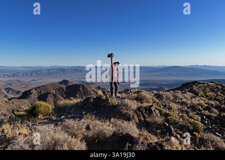 Donna in cima al Needle Peak nel Parco Nazionale della Valle della morte che tiene il registro della cima sopra la sua testa in trionfo con il cielo blu copyspace Foto Stock