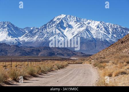 La strada di scogliera di ghiaia gesso si snoda attraverso la Valle di Owens, nella California orientale, verso il Monte Tom innevato nelle montagne della Sierra Nevada Foto Stock