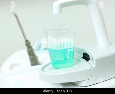 Moderne attrezzature di clinica dentale che dispensano collutorio turchese antisettico in una tazza usa e getta, promuovendo la salute e l'igiene orale Foto Stock