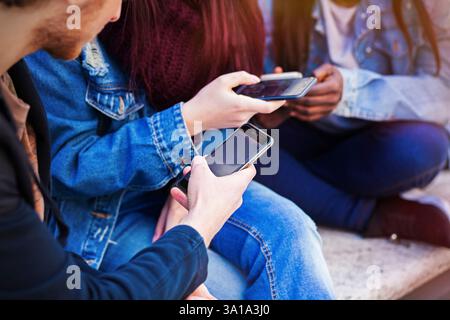 Tre giovani utilizzando il telefono cellulare. Concetto di amicizia in tempi moderni. Foto Stock