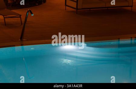 Rilassatevi in una piscina illuminata di notte, le sue acque blu scintillanti sotto le luci soffuse, creando un'oasi di pace perfetta per rilassarsi e fuggire dal trambusto quotidiano Foto Stock