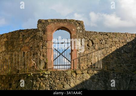 Porta a reticolo fatta di barre di ferro su un vecchio muro di pietra del castello con cielo nuvoloso Foto Stock