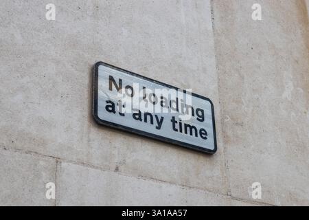 Cartello di divieto di carico in qualsiasi momento su un muro di pietra indicante le limitazioni di parcheggio e scarico Foto Stock