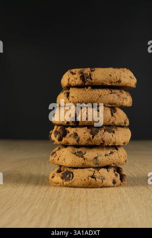 Una pila di biscotti con scaglie di cioccolato su un tavolo di legno. I biscotti sono impilati uno sopra l'altro, creando un'esposizione visivamente accattivante e deliziosa. Foto Stock
