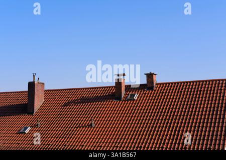 Primo piano del tetto di una casa con piastrelle. Il tetto è dotato di tegole standard e camini in mattoni di diverse dimensioni. Foto Stock