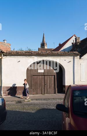 Una donna cammina davanti a un grande cancello ad arco in legno a Sibiu, Romania Foto Stock