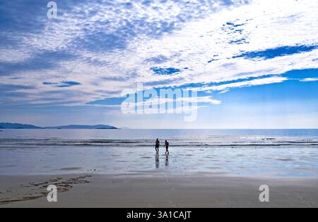 Due giovani uomini che si riflettono sulla sabbia bagnata, camminano sul bordo delle acque di Oldershoremore Beach, Sutherland, Highlands scozzesi, calmo pomeriggio estivo. Foto Stock