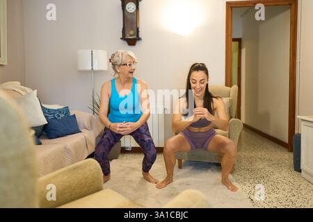 Personal trainer che assiste una donna anziana che fa gli squat a casa Foto Stock