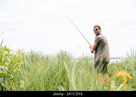 Uomo positivo e bello con gli occhiali da sole sta pescando all'aperto. Foto Stock
