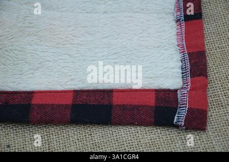 Una foto ravvicinata del bordo sui lati superiore e inferiore di una coperta di feltro bianca con un bordo a quadri rosso e nero. Foto Stock