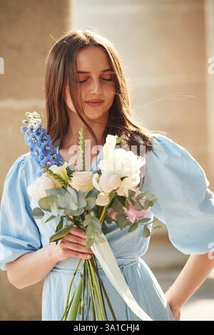 In piedi accanto a colonne di cemento. Bella donna è con i fiori nelle mani all'aperto. Foto Stock