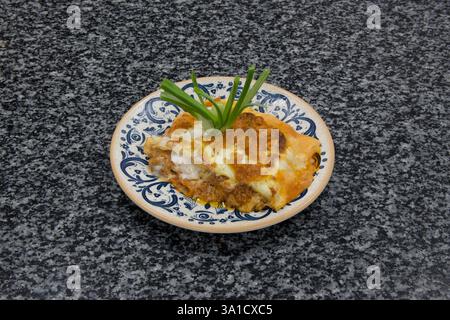 Un piatto di cibo con una foglia verde sopra. Il piatto è blu e bianco. Il cibo è una lasagna Foto Stock