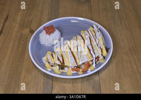 Un piatto di cibo con burrito e riso sopra. Il burrito è ricoperto da una salsa gialla Foto Stock