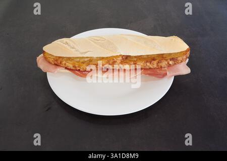 Un panino è su un piatto bianco. Il panino viene tagliato a metà e posto su un tavolo nero Foto Stock