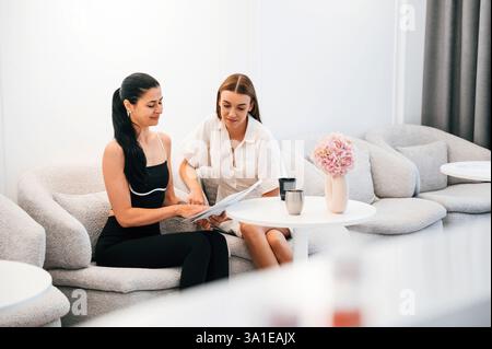 Due donne sono sedute sul divano e leggono i documenti. Foto Stock