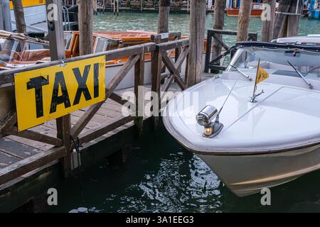 Venezia, Italia - 12 ottobre 2024: Un taxi d'acqua bianca ormeggiato in un molo di legno con un cartello giallo per taxi Foto Stock