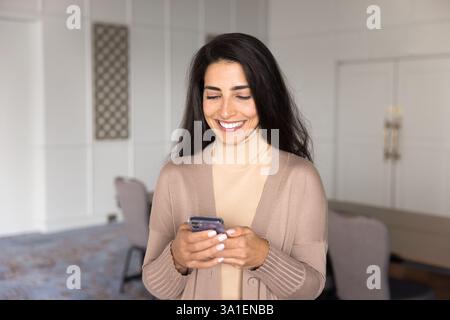 Donna d'affari brasiliana sorridente che usa lo smartphone in ufficio Foto Stock