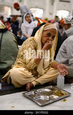 Delhi, India - 21 febbraio 2025: Donna che mangia lenticchie a un pasto comunale di Langar nel tempio Gurudwara Bangla Sahib Sikh Foto Stock