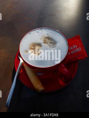 Cappuccino in una tazza rossa, la fotografia cattura una tazza di caffè rossa piena di un cappuccino schiumoso, seduto su un piattino rosso corrispondente. Foto Stock