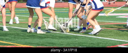 L'azione dinamica si svolge mentre più giocatori lottano per la palla durante una partita di lacrosse in una giornata di sole. Foto Stock