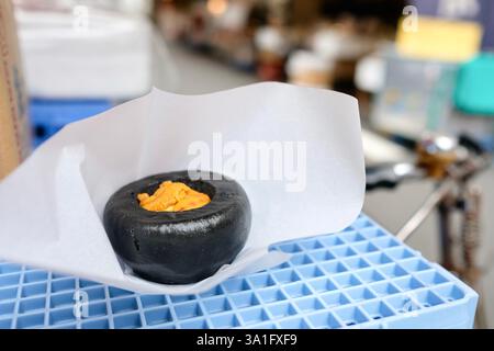 Panino di ricci di mare al vapore di Hamada Shoten, sopra una cassa di plastica blu al mercato del pesce esterno di Tsukiji a Chuo, Tokyo, Giappone Foto Stock