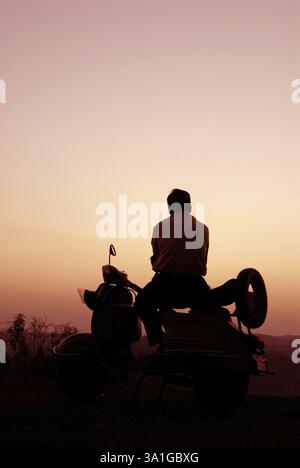 Uomo seduto sullo scooter che guarda il tramonto, la silhouette, la vista dalla cima di Parshuram Ghat, Chiplun, regione di Konkan, distretto di Ratnagiri, Maharashtra, India, A. Foto Stock