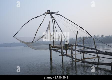 Fisherman in piedi sulla piattaforma della rete cinese che osserva le acque calme vicino a Bolgatty Island la mattina presto Ernakulam, Kerala, India, Asia Foto Stock