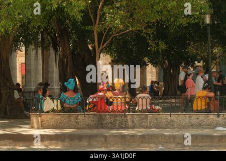 Havana, Cuba 2024 Apr17 - gruppo di donne cubane vestite con abiti tradizionali colorati chiamati Rumba, sedute in un parco sotto gli alberi vicino a un museu Foto Stock