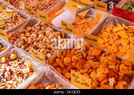 Vari tipi di frutta secca, tra cui fichi, albicocche, ananas e pere, sono esposti in vassoi rivestiti in plastica con cartelli etichettati in un mercato all'aperto Foto Stock