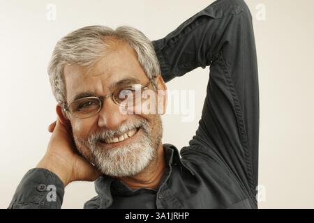 Vecchio dell'India del sud degli anni cinquanta con capelli grigi e barba che indossa camicia blu scuro e occhiali completamente rilassanti e sorridenti Foto Stock