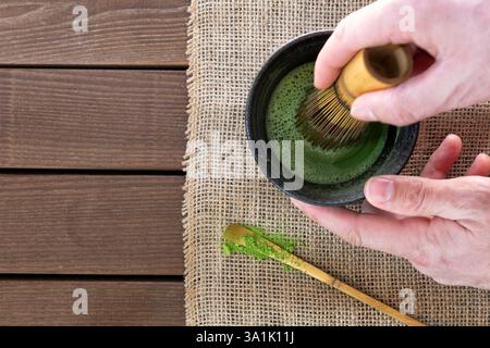 uomo che prepara tè matcha con frusta di bambù al tavolo di legno, vista dall'alto Foto Stock