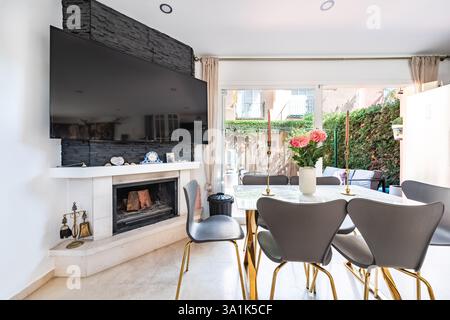 un'immagine ravvicinata di un tavolo da pranzo accanto al caminetto e alla televisione appesa nella casa vacanze mediterranea Foto Stock