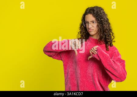 Non mi piace. Infelice ragazza caucasica che mostra un gesto di segno con il pollice giù, esprime malcontento disapprovazione, feedback negativo insoddisfatto. Bambino adolescente insoddisfatto in casa isolato su sfondo giallo Foto Stock