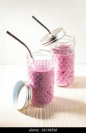 Bevanda rinfrescante e salutare. Frullato di mirtilli in due bicchieri con cannucce metalliche su bianco. Frullato con antiossidanti, frullato Foto Stock