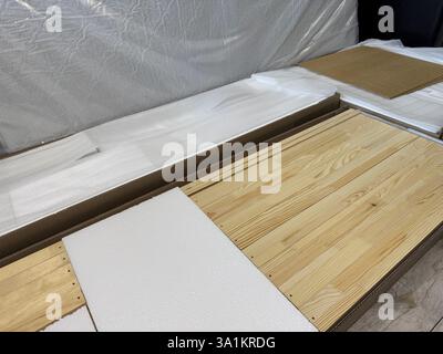 Un set di elementi per assemblare un ottomano. Spranghe di legno in imballaggi, distese sul pavimento. Nelle vicinanze si trovano materassi ortopedici. Foto Stock