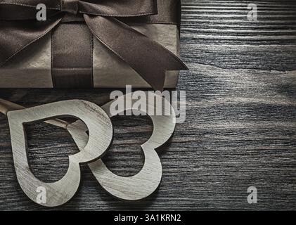Presenta una scatola con fiocco legato cuori di legno bianco su un concetto vintage di festa in legno Foto Stock