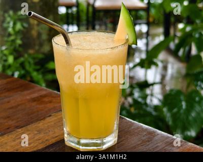 Un succo di melone frullato a freddo guarnito con una fetta di melone e una cannuccia di metallo riutilizzabile Foto Stock