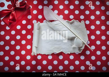 Presenta la confezione in rotolo di carta vintage con piume su tovaglia rossa a pois per festeggiare Foto Stock