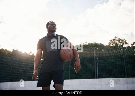 Persona sicura di sé. Il giovane nero è con la palla da basket all'aperto. Foto Stock