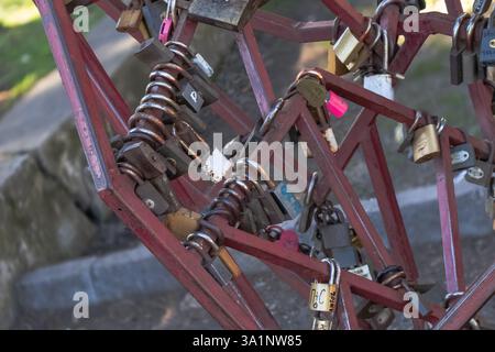 Lucchetti colorati sono appesi a una scultura in metallo a forma di cuore, a simboleggiare l'amore e l'impegno. Il caldo sole pomeridiano proietta ombre morbide, migliorando il Foto Stock