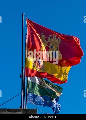 La bandiera rossa di Alora con castello giallo vola accanto alle bandiere spagnole, andaluse e UE contro il cielo blu Foto Stock