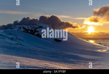 Un paesaggio invernale mozzafiato con colline innevate sotto un vibrante tramonto. Il sole proietta un caldo bagliore sul terreno ghiacciato, con un'impressionante clo Foto Stock