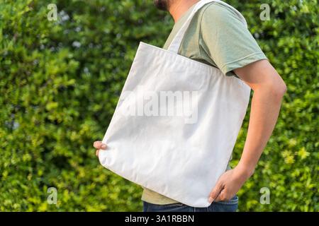 L'uomo sta tenendo in mano il tessuto di tela della borsa per il modello vuoto del mockup. Borsa tote in tessuto sacchetto per la spesa con mockup isolato. Sacchetto riutilizzabile in cotone Eco Products. Zero Foto Stock