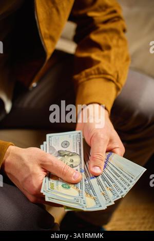 Primo piano di un uomo che conta banconote da un dollaro a casa. Persona che pianifica le sue finanze personali, seduto sul divano con soldi in contanti. Concetto di pianificazione casa bu Foto Stock