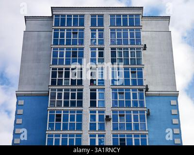 Vista diagonale dal basso del tipico edificio di appartamenti a piu' piani dipinto di blu contro un cielo blu. Concetto di crescita delle grandi città a causa dell'incre Foto Stock
